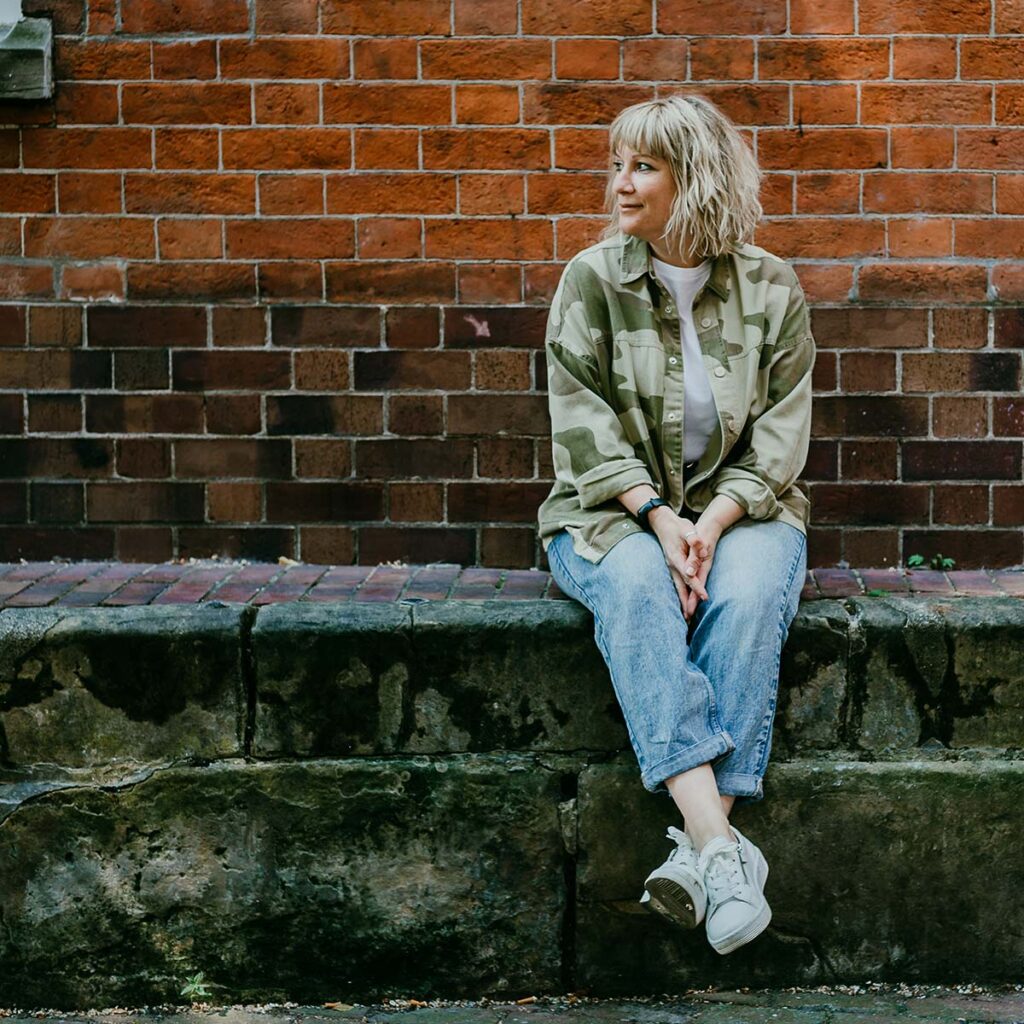 International Headshot & Brand Photographer, Gemma Wilks, sitting on a wall in Nottingham's Lace Market