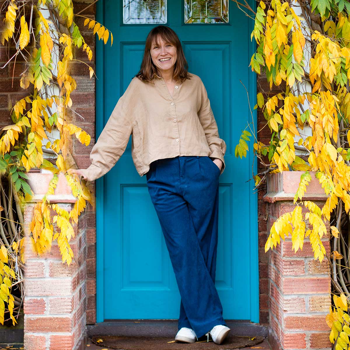 Interior Designer stood in front of a her bright blue door with autumnal leaves surrounding