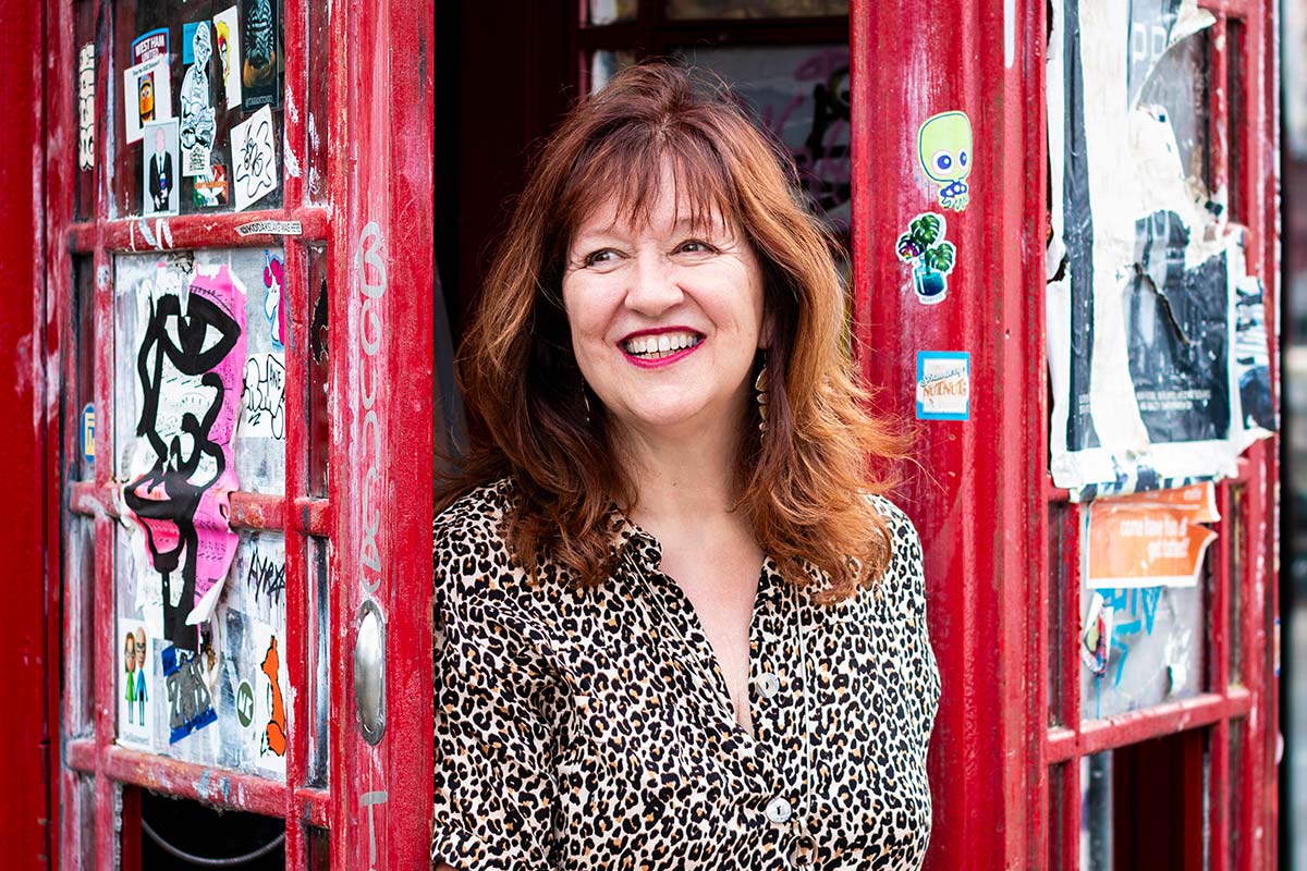 Headshot of Gill McKay, Sobriety Coach, stood in the door of a red telephone box in Spitalfields, London